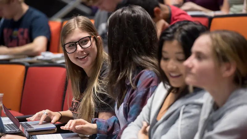 A group of students in a classroom talking and laughing. 