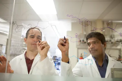 Two lab partners writing equations on glass